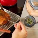 Digital meat thermometer next to grilled steak on wooden board