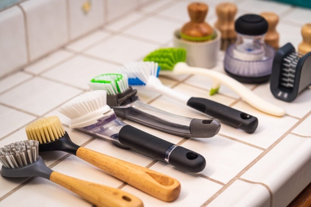 Modern dish brush and scrubber next to a clean sink with soap suds.